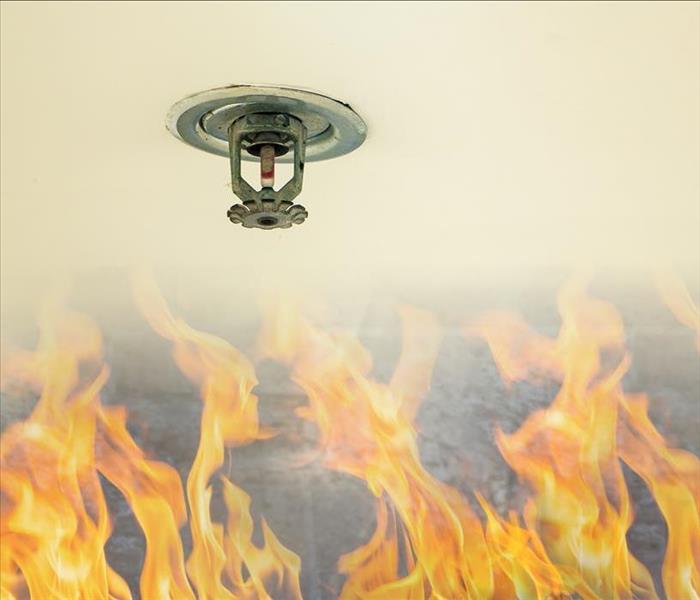 Fire sprinkler head on white ceiling in a building, with flames